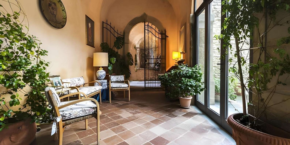 A sunlit room with a tiled floor, a wooden chair, a table, a lamp, and a large potted plant. 3