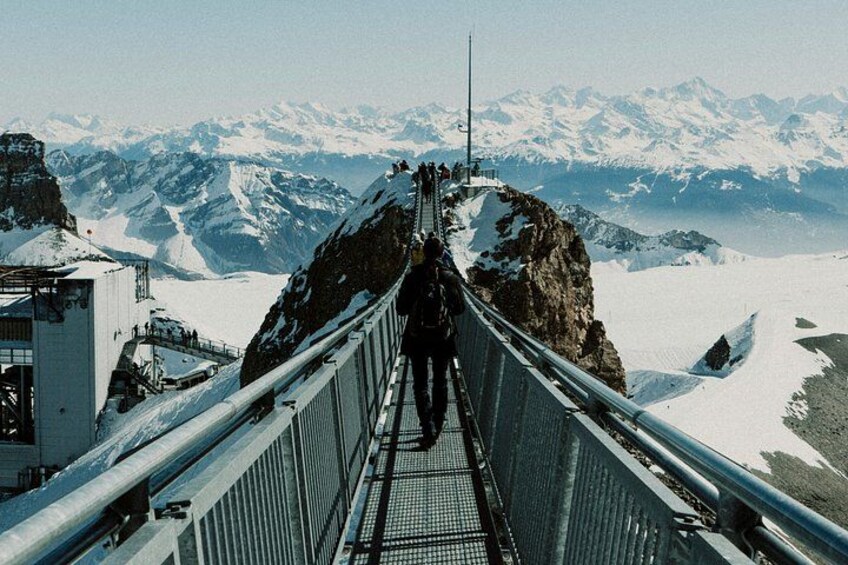 A metal bridge with railings, snow-covered mountains in the background, and a person standing at the end. 3