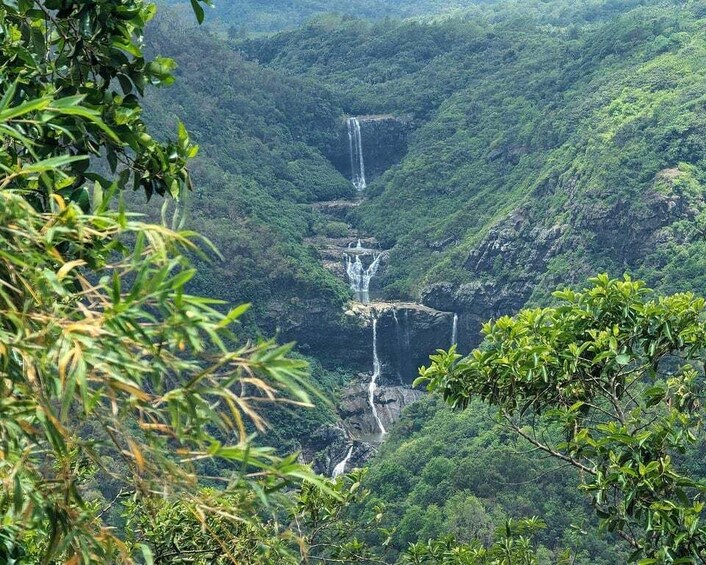 A multi-tiered waterfall cascading through a lush, green valley surrounded by dense foliage. 1