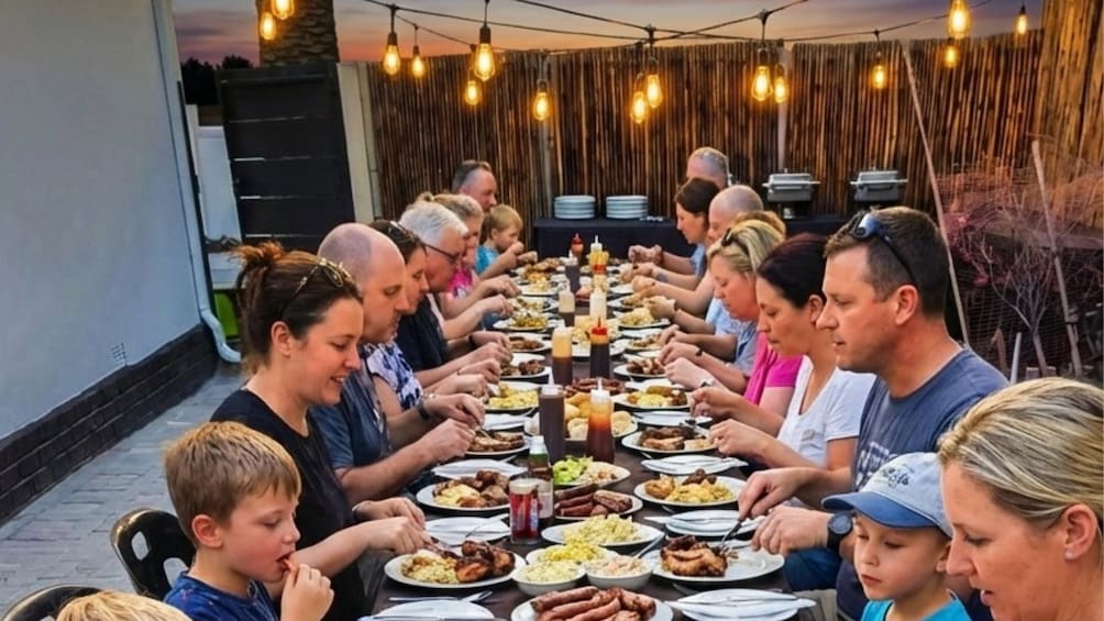 Un grupo de personas sentadas alrededor de una mesa larga con diversos platos, bajo luces colgantes. 1
