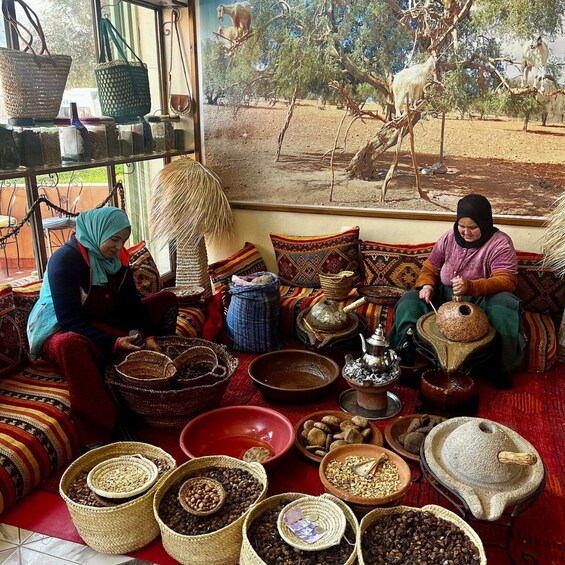Two women seated on a patterned sofa surrounded by various containers of coffee beans and traditional coffee-making equipment. 5