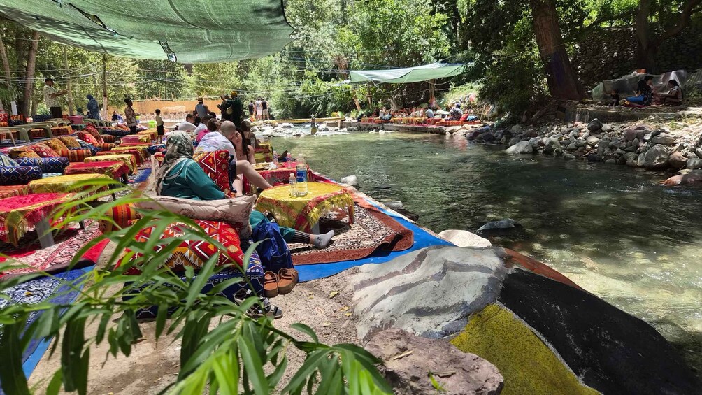 A riverside market with colorful textiles and people sitting by the water. 2