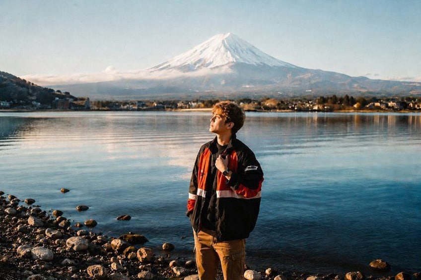 A person standing by a calm lake with a snow-capped mountain in the background. 1