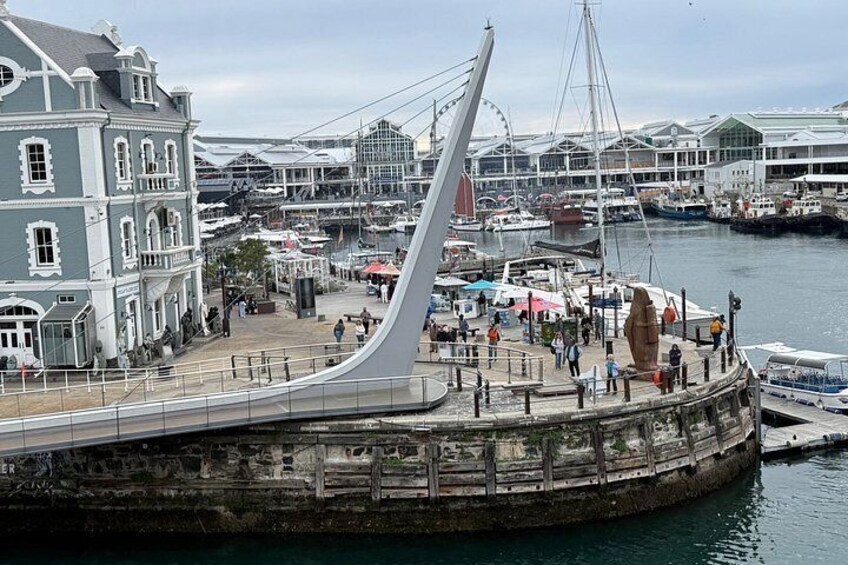 A waterfront promenade with a modern bridge, historic buildings, and a marina with boats. 3