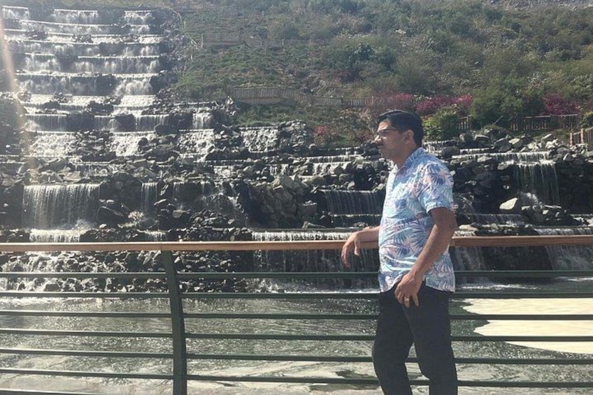 A man standing by a tiered waterfall with a railing in the foreground. 2