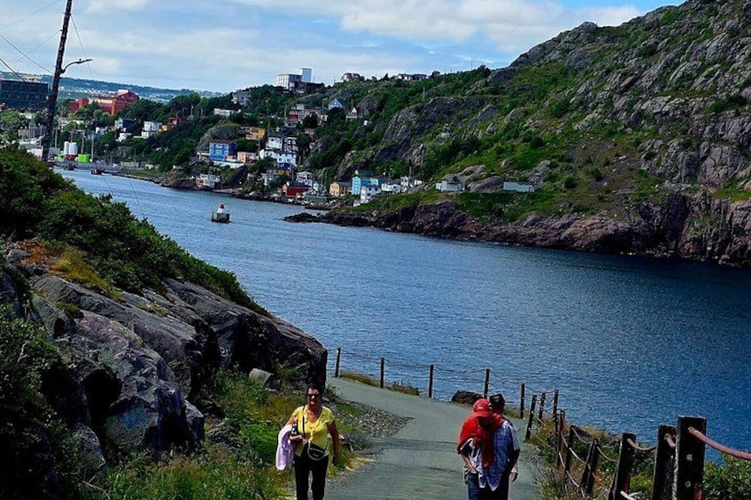 A coastal town with a river, a person walking on a path, and a boat in the water. 4