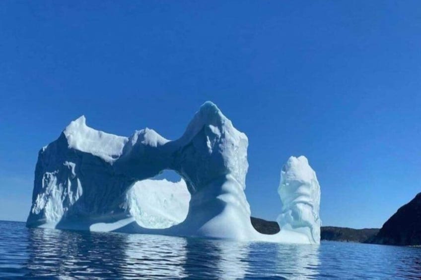 An iceberg with a large opening, surrounded by calm water and clear skies. 2
