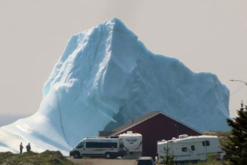 A large iceberg in front of a red building with a white RV and a truck parked nearby. 4
