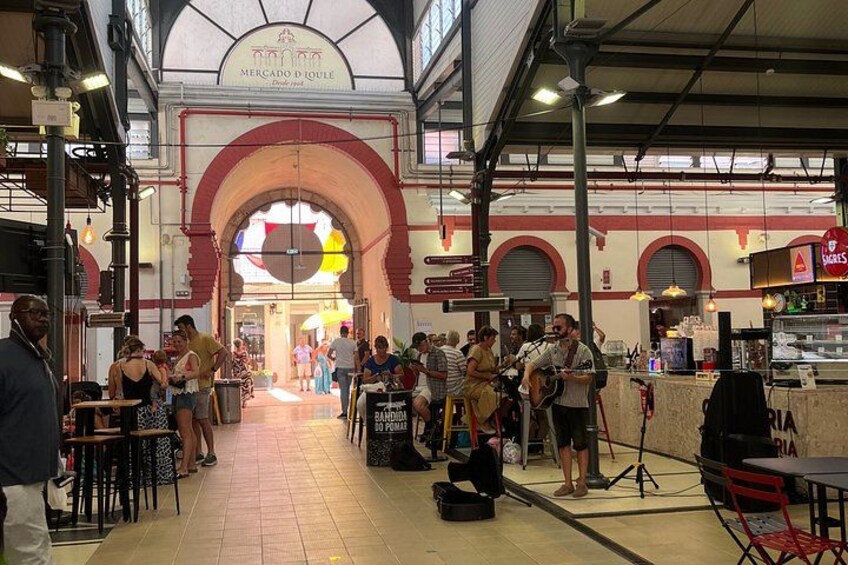 A busy indoor market with people shopping and a musician performing. 2