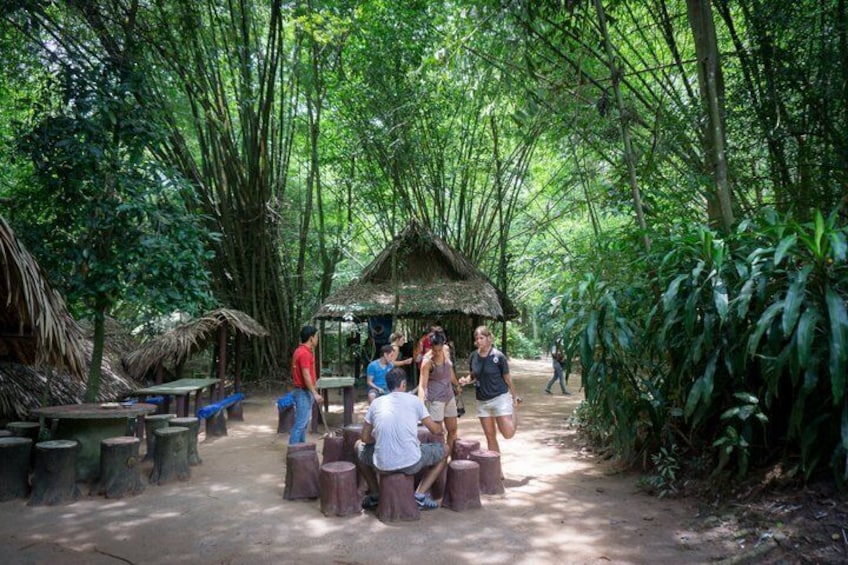 A group of people gathered around a thatched-roof structure in a bamboo forest. 1