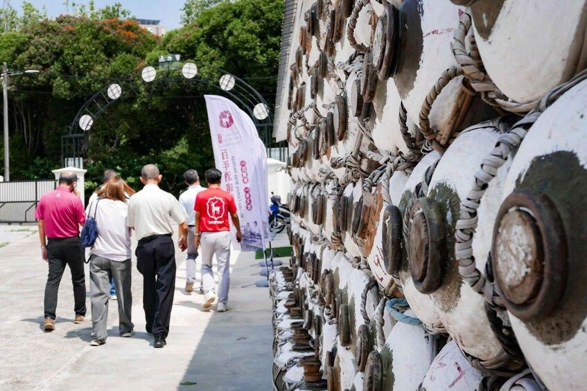 A group of people walking past a wall of old, rusted metal parts. 5