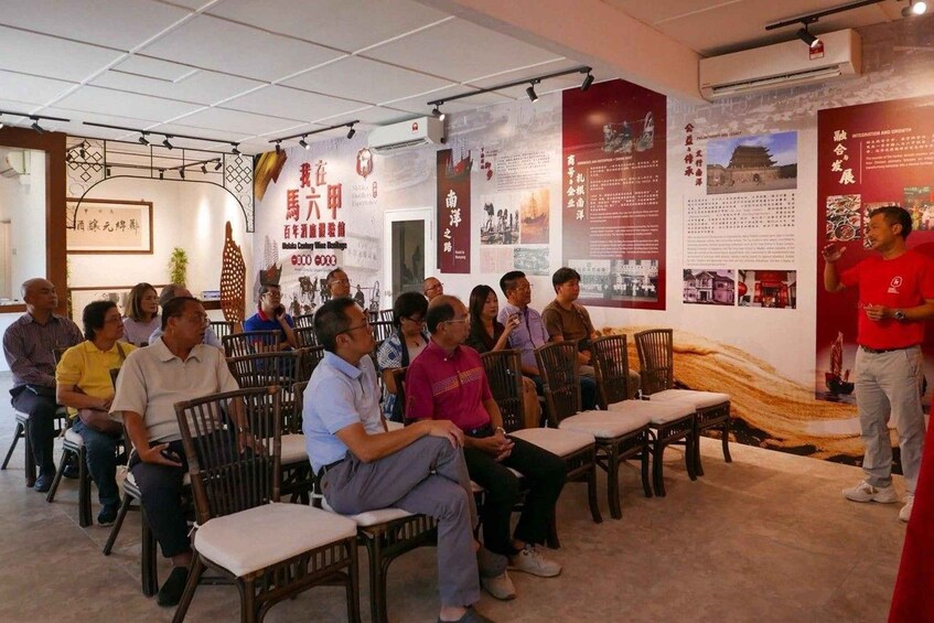 A group of people seated in a room with informational posters on the walls. 1