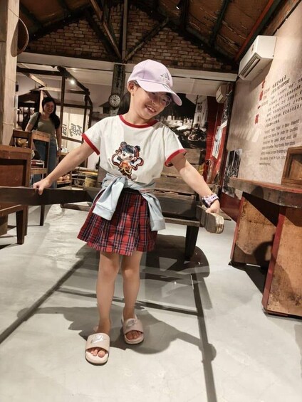 A person in a plaid skirt and white t-shirt with a cartoon character, standing in a room with brick walls and wooden furniture. 4