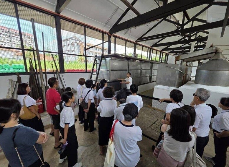 A group of people observing a large industrial machine in an indoor facility with metal beams and large windows. 5