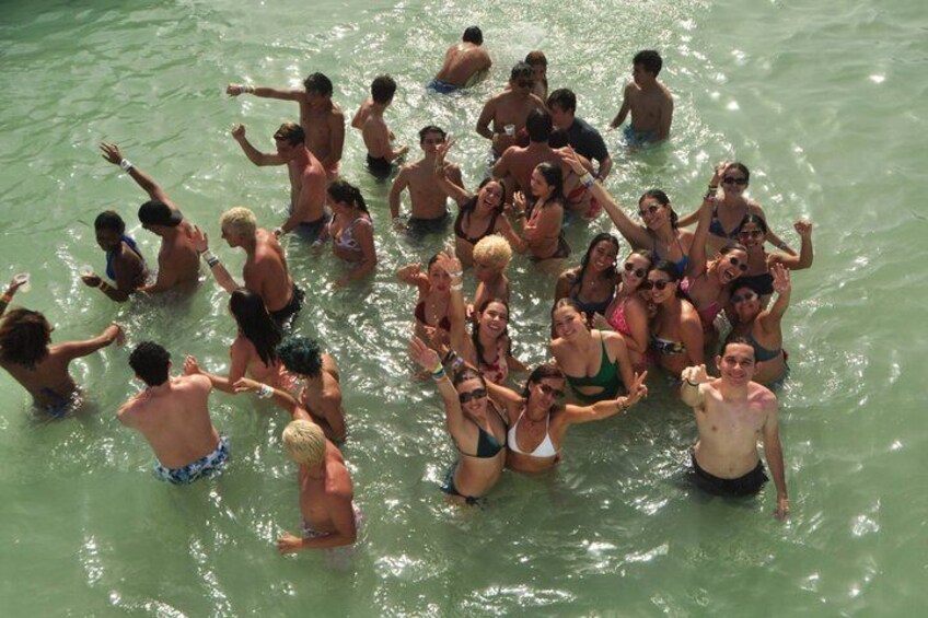 A group of people in a body of water, some standing and some sitting, with a few individuals in the water. 5