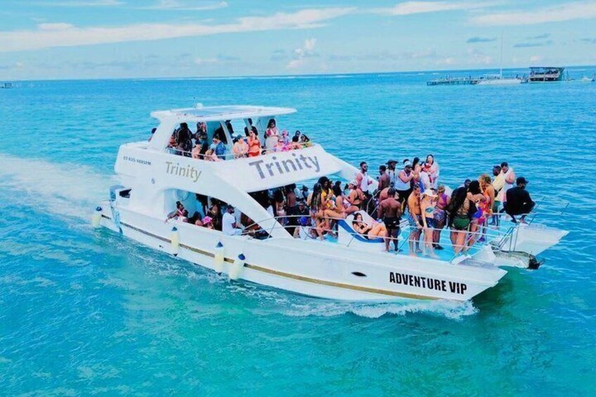 A white boat named 'Trinity' with 'Adventure VIP' written on the side, filled with people on a clear day. 1