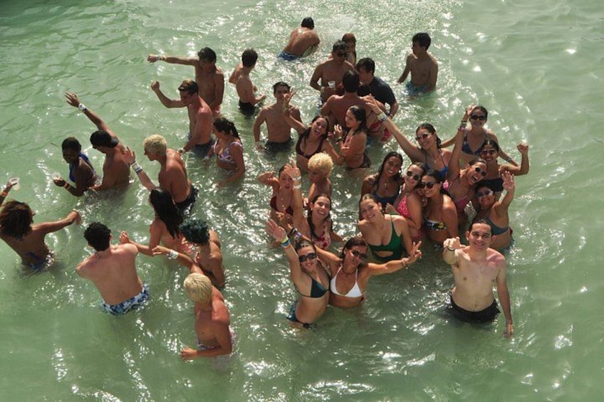 A group of people in a body of water, some standing and some sitting, with a few individuals in the water. 4