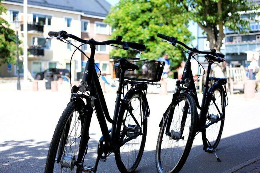 Two bicycles parked on a sidewalk with a building and trees in the background. 2
