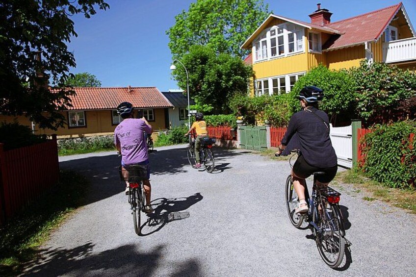 Three cyclists on a paved road with houses and greenery in the background. 3