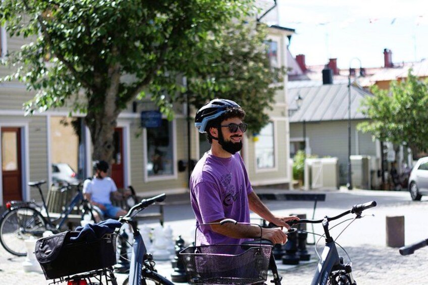 A person on a bicycle with a basket, parked on a street with buildings and trees in the background. 4