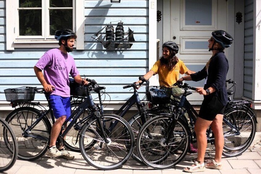 Three people standing next to bicycles in front of a house with a white door and a window. 4
