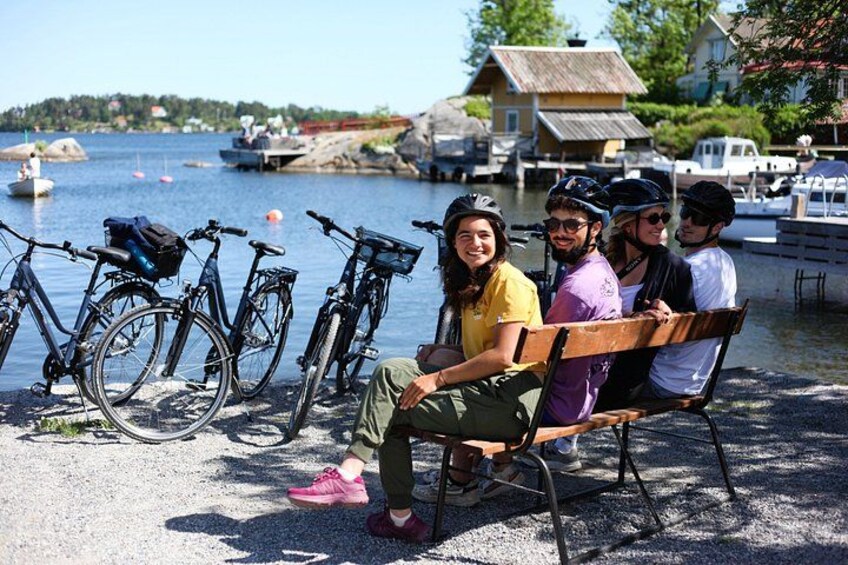 A group of people sitting on a bench by a waterfront with bicycles parked nearby. 5