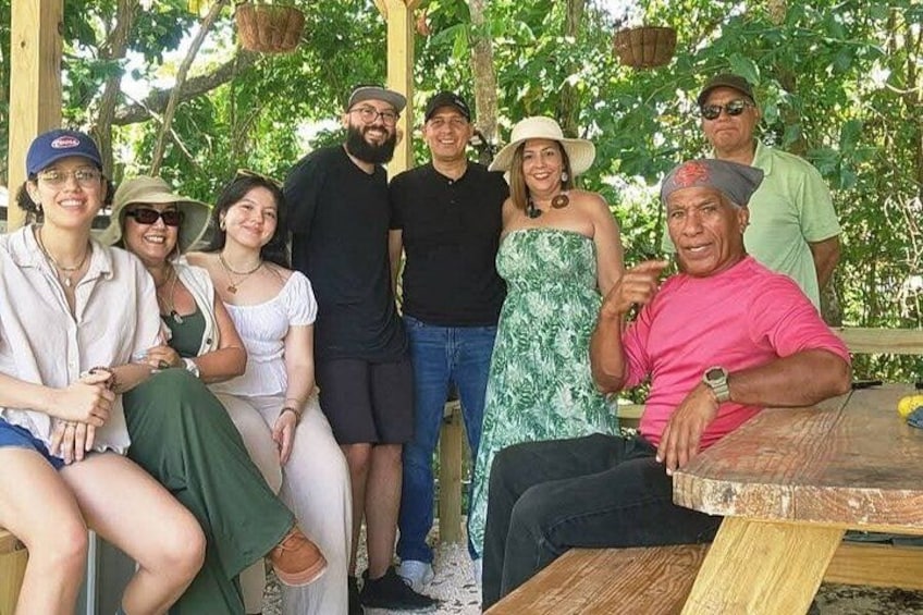 A group of people sitting and standing outdoors under a wooden structure with hanging baskets. 3