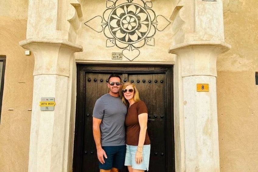 A couple standing in front of a building with a large door and a decorative emblem above it. 5