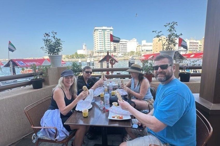 A group of people dining at an outdoor table with a cityscape and water in the background. 1