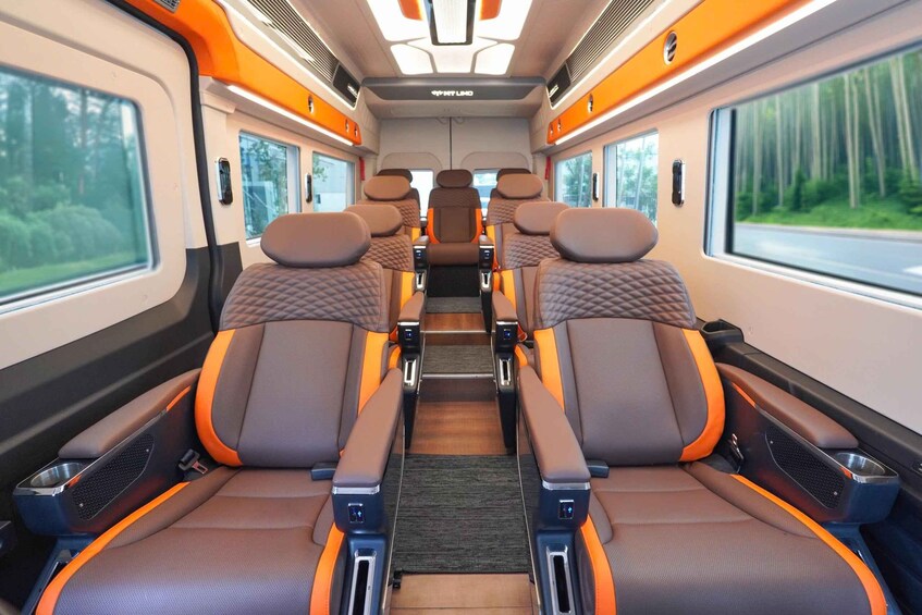 A train interior with brown and orange seats, overhead luggage racks, and large windows. 5