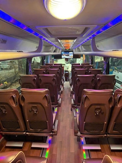A bus interior with rows of seats, overhead lighting, and a digital display. 2