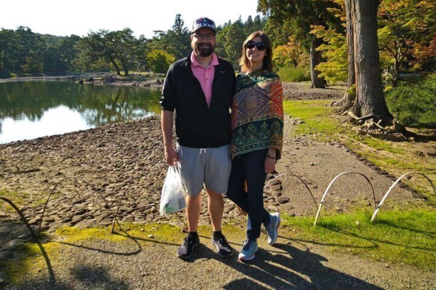 Two people standing by a lake with a rocky shore and trees in the background. 1