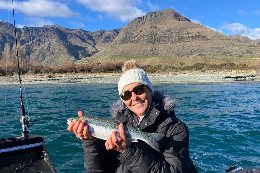 A person holding a fish on a boat with mountains in the background. 5