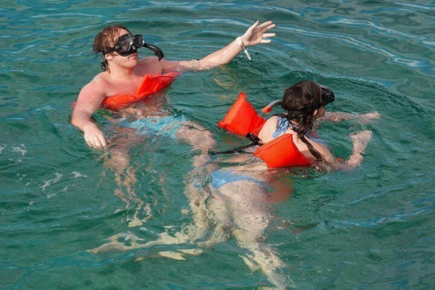 Two people snorkeling in clear water, wearing red life vests. 5
