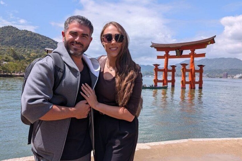 A couple standing by a body of water with a traditional Japanese torii gate in the background. 3