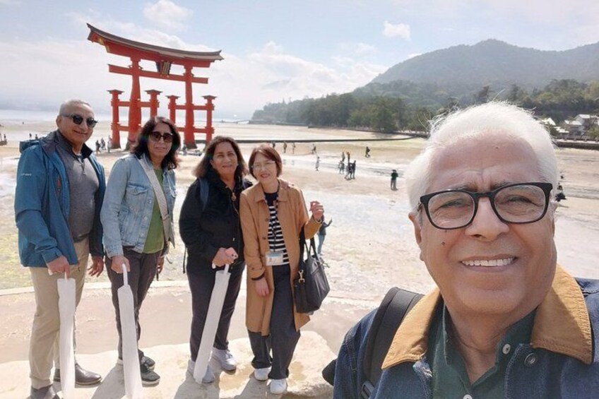 A group of people standing in front of a red torii gate with a mountainous landscape in the background. 4