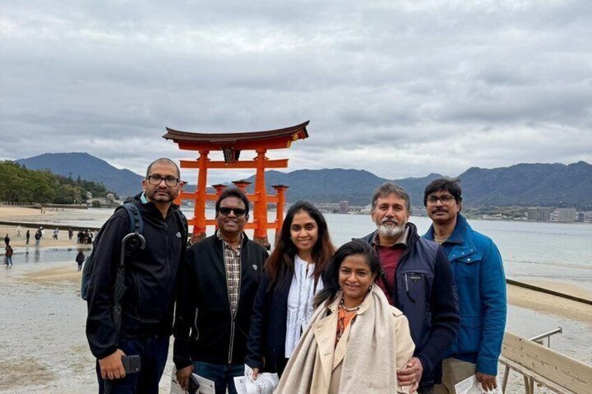 A group of people standing in front of a red torii gate with a body of water and mountains in the background. 5