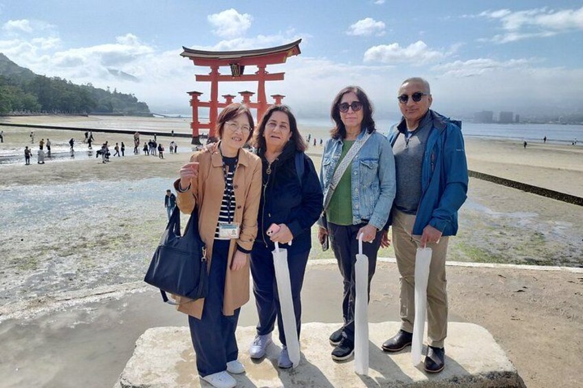 A group of people standing in front of a red torii gate at a beach with a clear sky. 5