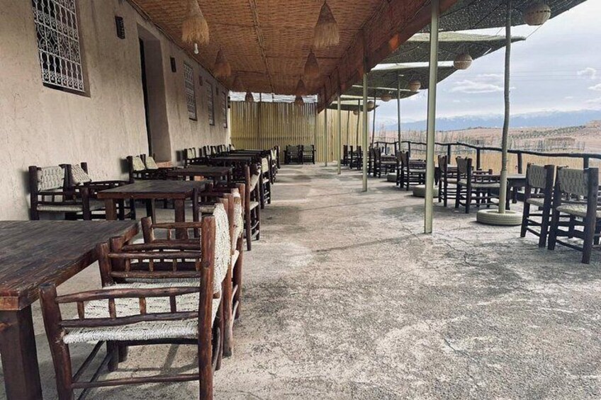 A covered outdoor seating area with wooden tables and chairs, a concrete floor, and a view of a mountainous landscape. 5