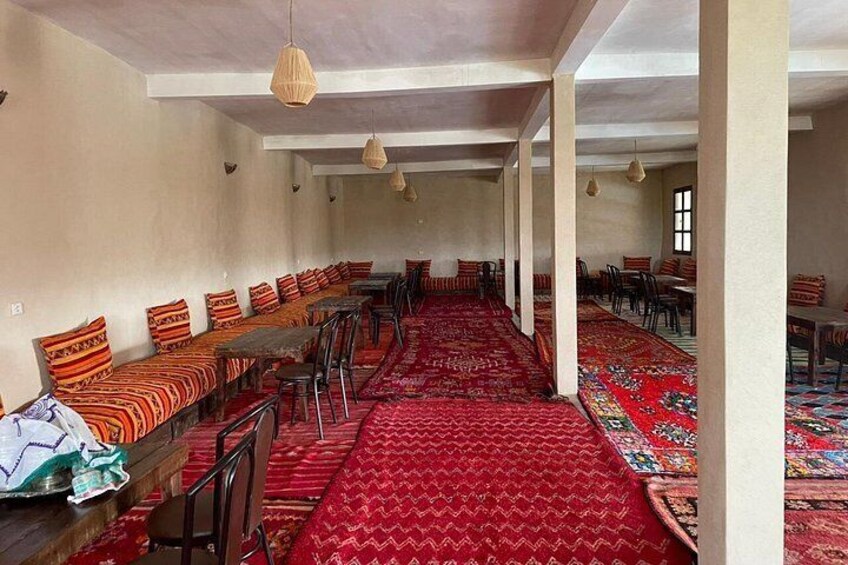 A room with rows of wooden benches and tables, red patterned carpets, and hanging pendant lights. 3