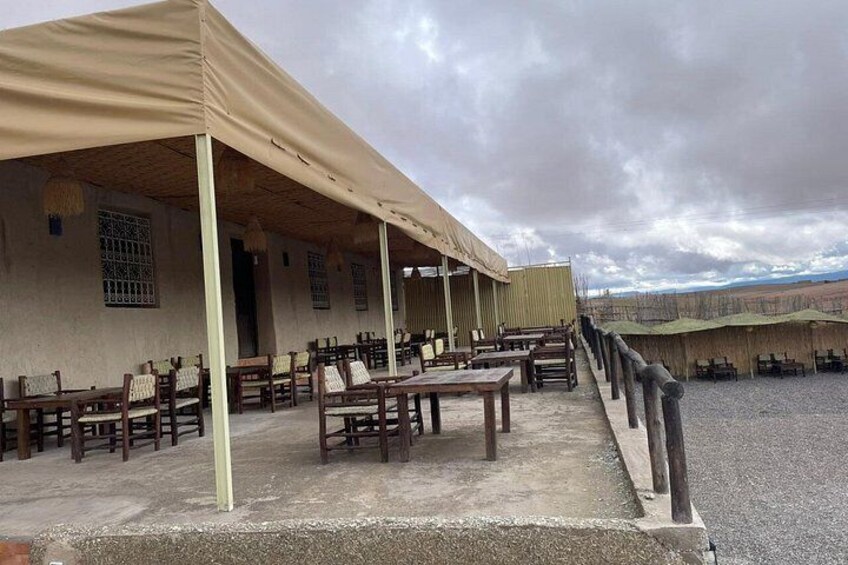 A covered outdoor seating area with tables and chairs, a gravel ground, and a distant view of a landscape. 4