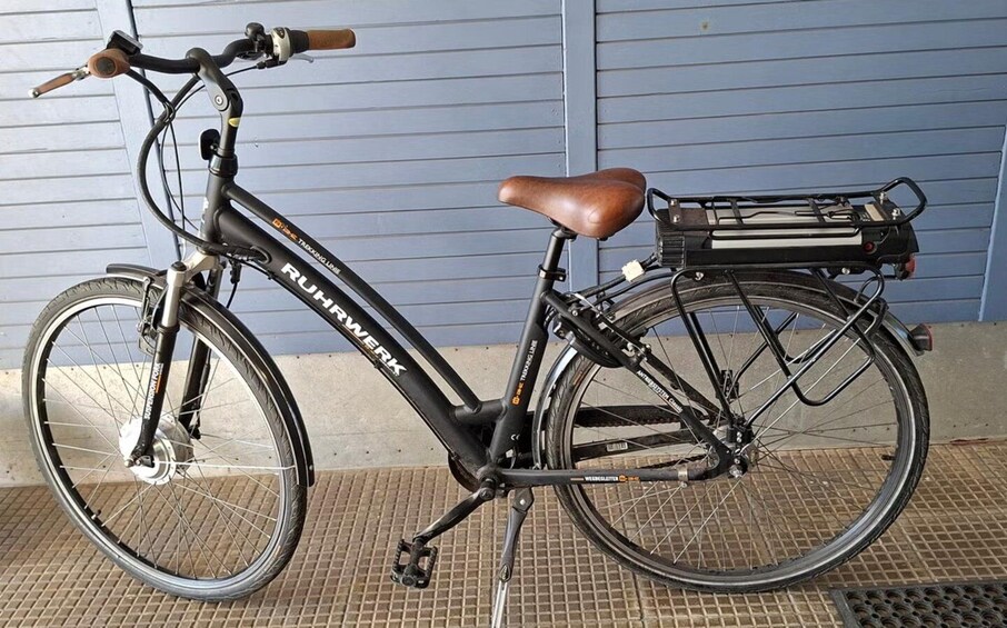 A black bicycle with a brown seat and a rear rack, parked against a blue wall. 3