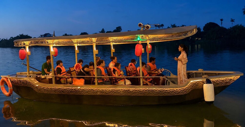 A traditional boat with passengers wearing life jackets, illuminated by lights, on calm water at dusk. 3