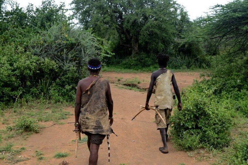 Two people walking on a dirt path surrounded by greenery. 5