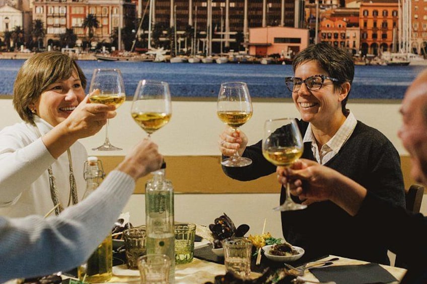A group of people toasting with wine glasses at a table with a view of a waterfront and buildings in the background. 1
