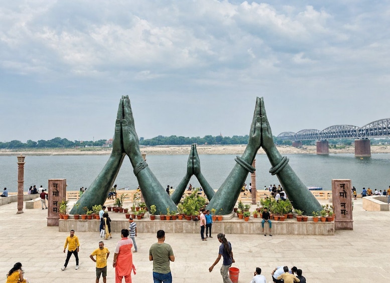 A river with a bridge in the background, a large sculpture of hands, and people around. 5