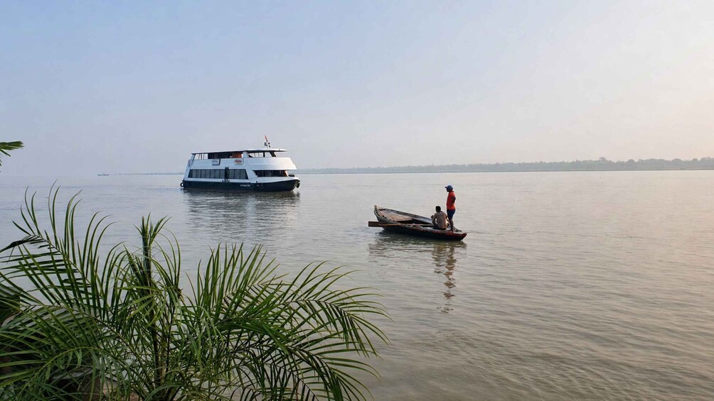 A large white boat on calm water with a person standing on a smaller boat nearby. 3