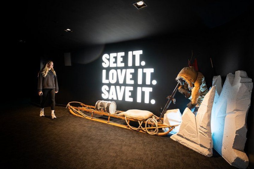 A person in a sled-like structure on a dark floor with a large illuminated sign in the background. 4