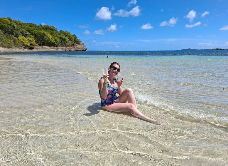 A person sitting on a beach with clear water, a distant shoreline, and a clear sky. 1