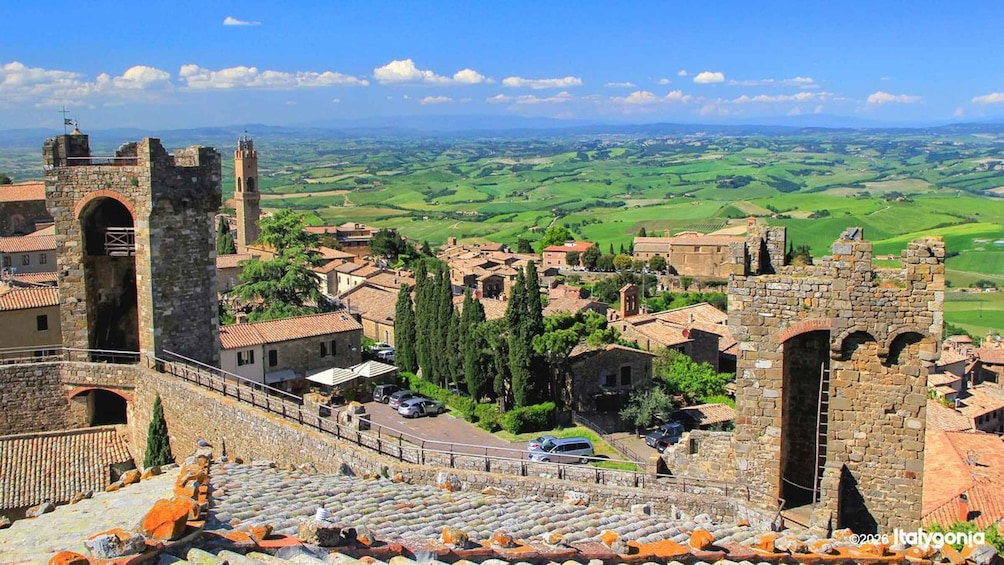 A historic town with stone architecture, a prominent tower, and terraced vineyards in the background. 1